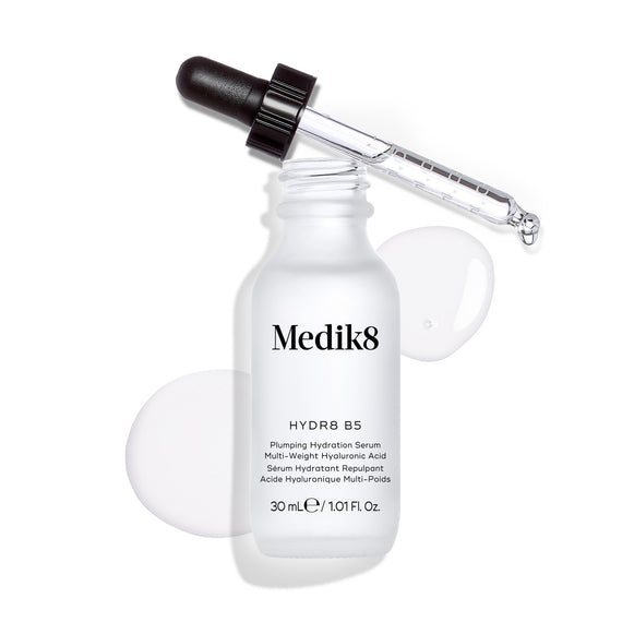 Frasco do sérum Medik8 Hydr8 B5 apresentado sobre um fundo branco limpo, com uma poça de líquido transparente e gotas à volta, com o conta-gotas apoiado no topo.-37