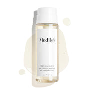 Medik8 Press & Glow – frasco sobre um fundo branco limpo com gotas de líquido translúcidas e uma pequena poça que realça a textura aquosa. O texto descreve o produto como um «Tónico PHA esfoliante diário com ativador de enzimas» de 200 ml.