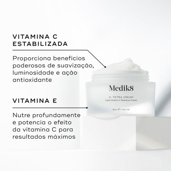 Um pote aberto de Medik8 C-Tetra Cream revelando o creme branco no interior, colocado sobre um bloco branco contra um fundo claro. O texto em português destaca os ingredientes principais: Vitamina C Estabilizada que proporciona benefícios poderosos de suavização, luminosidade e ação antioxidante, e Vitamina E que nutre profundamente e potencia o efeito da vitamina C para resultados máximos.-hover-16