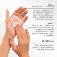 Close-up de mãos a esfregar uma espuma de limpeza branca contra um fundo claro. Linhas de texto destacam os ingredientes: AHAs (ácido mandélico e ácido láctico) para esfoliar células mortas e uniformizar a textura, BHAs (ácido salicílico) para desobstruir a pele para um tom mais limpo, e Glicerina para hidratar e deixar a pele macia.
