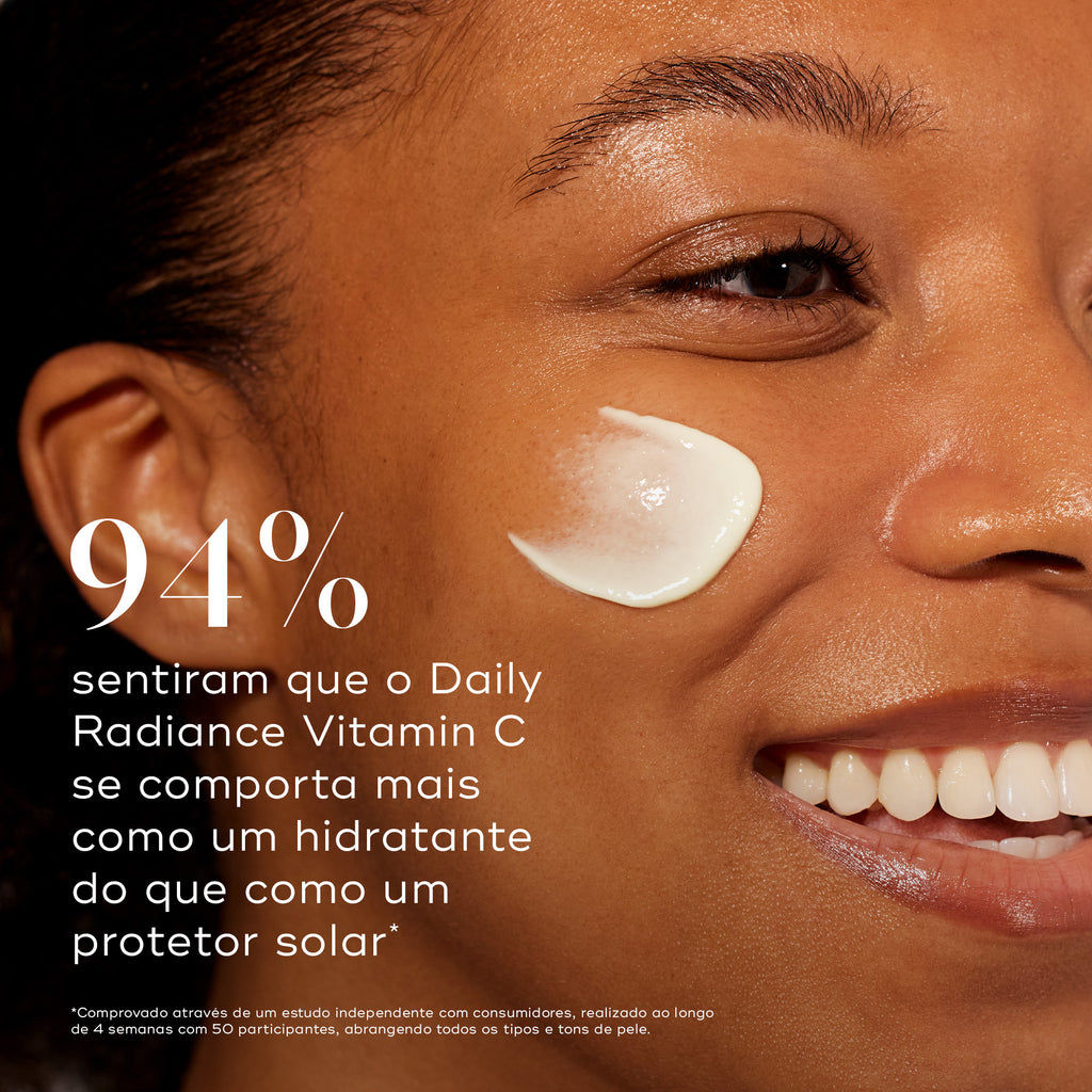 Um close-up de uma mulher sorridente com um pouco de creme na bochecha contra um fundo quente. Um texto grande afirma que 94% sentiram que o Daily Radiance Vitamin C se comporta mais como um hidratante do que como um protetor solar.