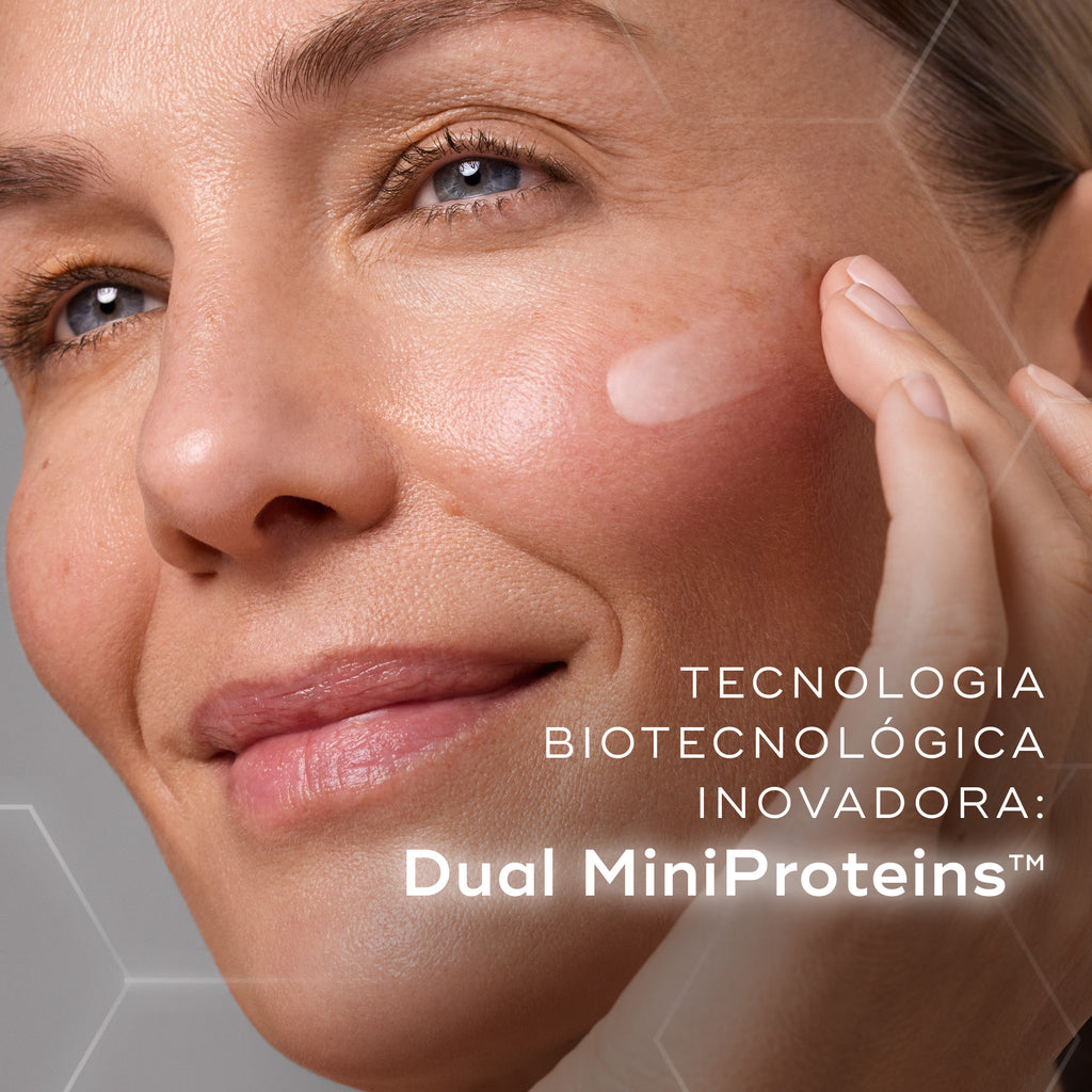 Primeiro plano de uma modella sorridente a aplicar uma porção de creme branco na bochecha contra um fundo com gráficos hexagonais subtis. O texto em português destaca a inovadora tecnologia biotecnológica: Dual MiniProteins™.