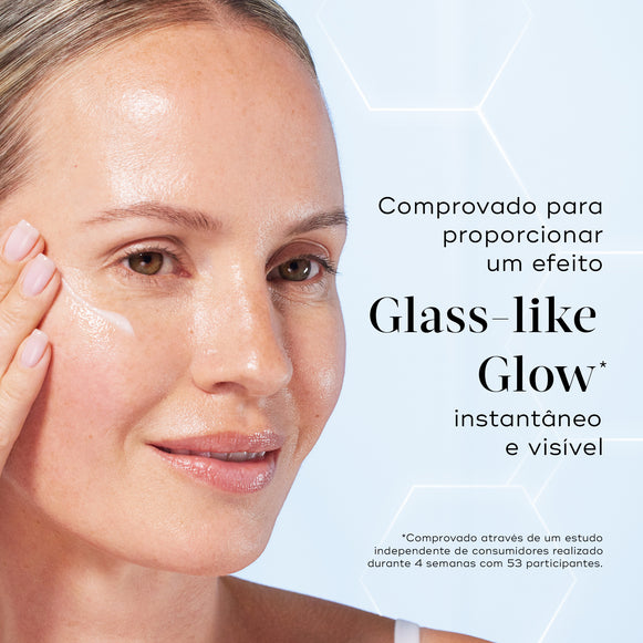 Primeiro plano de uma modella sorridente a aplicar uma porção de sérum branco na bochecha contra um fundo azul claro com gráficos hexagonais subtis. O texto em português destaca que o produto é comprovado para proporcionar um efeito Glass-like Glow instantâneo e visível.-hover-4