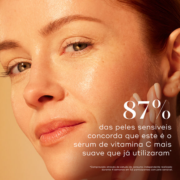 Um close-up de uma mulher tocando a sua bochecha luminosa contra um fundo bege quente. Um texto grande afirma que 87% dos utilizadores com pele sensível concorda que este é o sérum de vitamina C mais suave que já utilizaram.-hover-1
