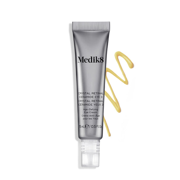 Bisnaga do creme Medik8 Crystal Retinal Ceramide Eye 3 ao lado de uma amostra em ziguezague de creme amarelo, sobre um fundo branco.-6