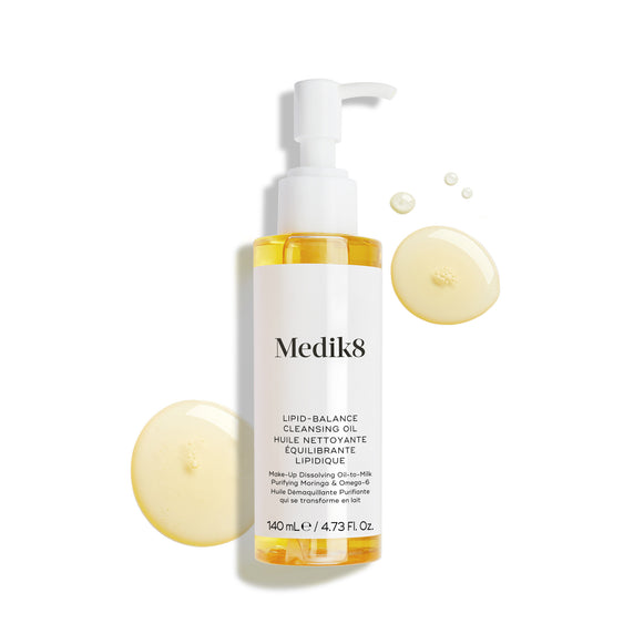 Frasco do Medik8 Lipid-Balance Cleansing Oil apresentado sobre um fundo branco. Gotas de óleo dourado envolvem o frasco, destacando a sua textura rica e fluida.-26