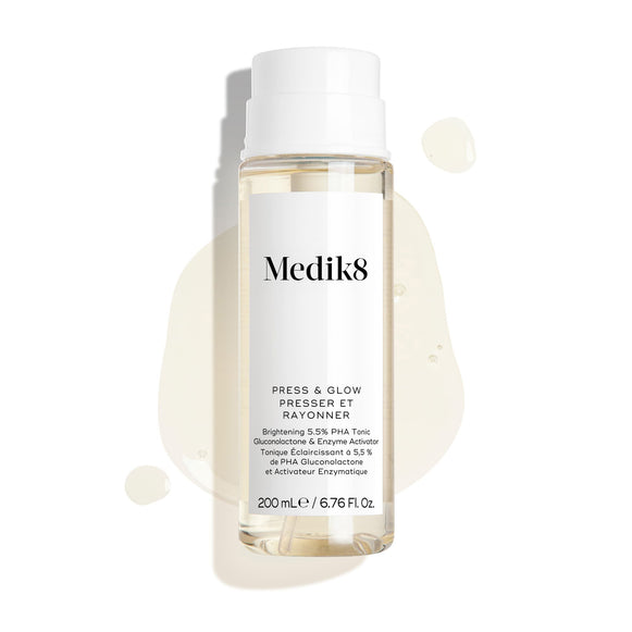 Frasco do tónico Medik8 Press & Glow apresentado sobre um fundo branco limpo, com gotas de líquido translúcidas e uma pequena poça, destacando a sua textura aquosa.-15